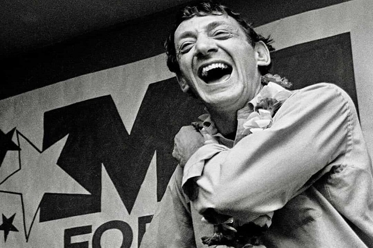 Quotes from Harvey Milk - Laughing joyfully in front of a "VOTE" campaign poster in a black and white photo.